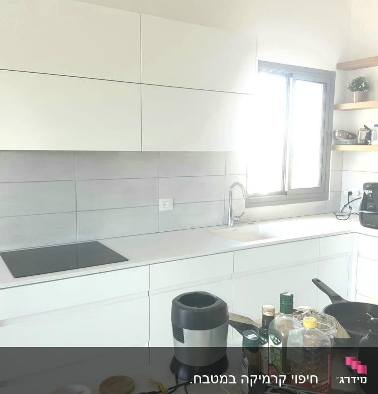 מטבח עם ארונות לבנים ומשטח עבודה, כיור וברז